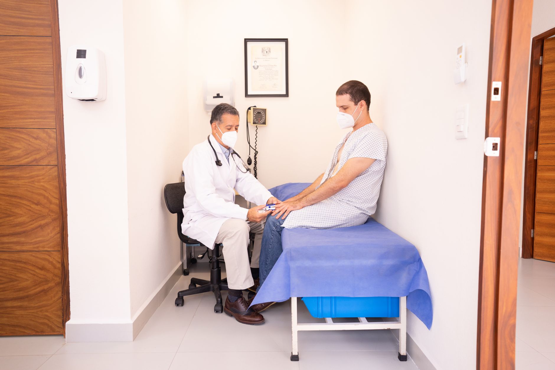 Persona pensativa evaluando sus síntomas, con un médico en el fondo, simbolizando la decisión entre consulta virtual y presencial.