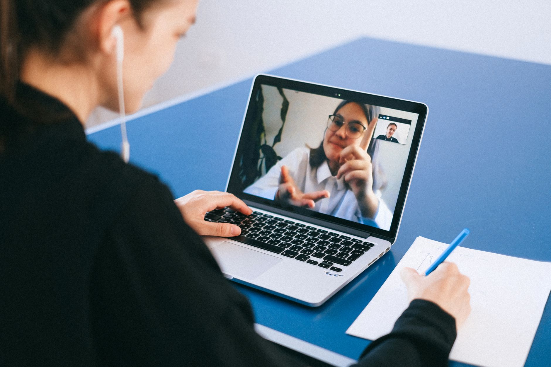 Una persona joven y atenta interactuando con una pantalla de computadora durante una consulta médica virtual, con un cuaderno y un lápiz a su lado.